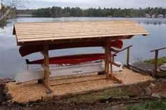 a red and white kayak sitting under a wooden shelter next to a body of water