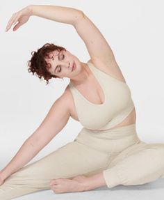 a woman is sitting on the floor in yoga gear and stretching her arms up with one hand