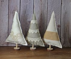 three small christmas trees made from fabric on wooden stand against a wood wall with lace trimming around them