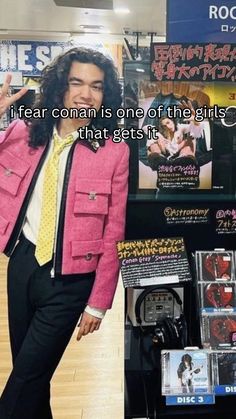 a man with long hair wearing a pink jacket and tie standing in front of a store display