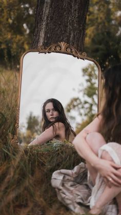 a woman sitting on the ground in front of a mirror looking at her face and body