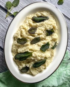 mashed potatoes with sage leaves in a white bowl on a green napkin and wooden table