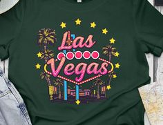 Embrace the vibrant essence of Las Vegas with this fun and stylish graphic tee featuring a retro Las Vegas sign. Perfect as a souvenir from your trip or a unique gift for a friend who loves the city that never sleeps! The colorful design adds a touch of excitement to any casual outfit, capturing the spirit of Las Vegas. This t-shirt is a great addition to your wardrobe and a perfect conversation starter. Wear it on your next casual outing, trip to the city, or as a reminder of your adventures in Las Vegas. Retro Green T-shirt For Fans, Retro Green T-shirt For Fan Merchandise, Retro T-shirt With Custom Print For Fan Merchandise, Retro Custom Print T-shirt For Fans, Retro Custom Print T-shirt For Fan Merchandise, Retro Multicolor Custom Print T-shirt, Retro Multicolor T-shirt With Custom Print, Vintage Multicolor Text Print T-shirt, Retro Las Vegas