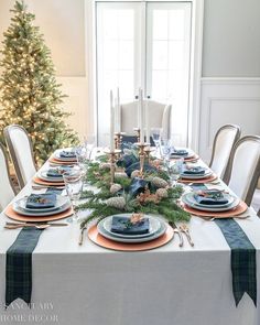 a dining room table set for christmas with blue and white plates, silverware, greenery and candlesticks