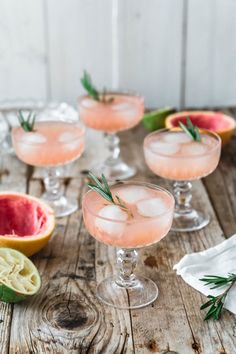 three glasses filled with pink lemonade and rosemary garnish next to sliced grapefruit