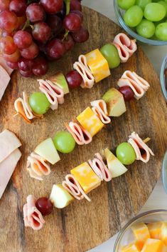 grapes, ham and cheese are arranged on skewers next to bowls of fruit