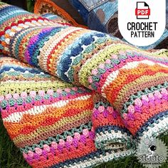 a crocheted blanket laying on top of grass next to a pair of jeans