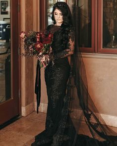 a woman in a long black dress holding flowers and wearing a veil with her hair pulled back