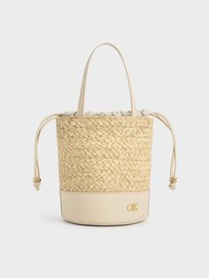 The quintessential bucket bag with a summer-friendly twist. This piece features a classic cylindrical shape, with a leather bottom offering a smooth contrast to the intricate woven finish and providing extra stability. It also includes a drawstring closure for quick and easy access to your belongings while keeping them safe and secure. The emblem adds a subtle touch of glamour in gold, further elevating this sophisticated design. Cheap Summer Cream Bucket Bag, Cheap Gold Bucket Bag, Leather Bucket Bag With Bamboo Handle In Natural Color, Natural Leather Bucket Bag With Bamboo Handle, Luxury Straw Bucket Bag With Woven Leather, Luxury Woven Leather Straw Bucket Bag, Leather Bucket Bag With Braided Handles In Basket Shape, Elegant Natural Bucket Bag With Bamboo Handle, Luxury Straw Bucket Bag With Bamboo Handle