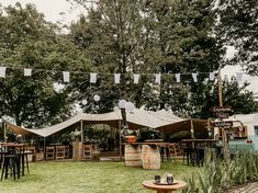 there are many tables and chairs outside in the yard with flags hanging from the trees