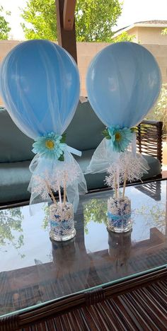 two blue balloons sitting on top of a glass table next to each other in vases