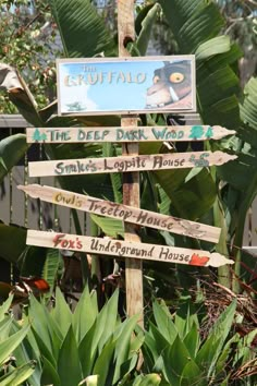 a wooden sign with many different signs on it in front of some plants and trees