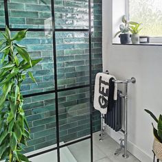 a bathroom with green tiles and plants in the window sill, along with a towel rack