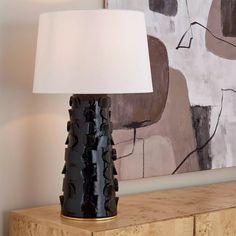 a black table lamp sitting on top of a wooden dresser next to a large painting