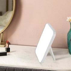 a table with a mirror, lipstick holder and vase on it next to a bed