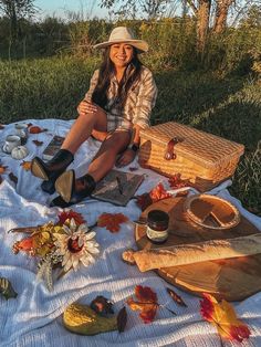 a woman sitting on top of a white blanket next to a basket and some food