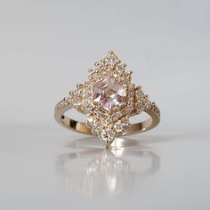 Inspired by the elegance and beauty of chandeliers, this morganite ring features a custom cut hexagon morganite center stone surrounded by natural white diamonds. Tiny white diamonds cascade down the ring band giving it a glamor effect. Made in 14k yellow gold, rose gold and white gold. This ring is handmade and designed in NYC. Materials: - 14K solid gold - 2.5 mm band thickness - 7x7mm custom cut natural hexagon morganite center stone - Natural white diamonds - SI1 clarity white diamonds. Appr Luxury Morganite Diamond Ring With Accents, Luxury Morganite Diamond Ring With Diamond Accents, Luxury Morganite Diamond Wedding Ring, Formal Morganite Diamond Ring With Accents, Formal Morganite Diamond Ring With Diamond Accents, Luxury Morganite Jewelry With Center Stone, Luxury Morganite Diamond Ring With Halo Setting, Blush Morganite Ring With Center Stone, Elegant Morganite Diamond Ring In White Gold