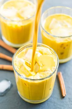 two glasses filled with yellow liquid and cinnamon sticks next to each other on a table