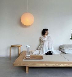 a woman sitting on top of a bed next to a table with a lamp hanging above it