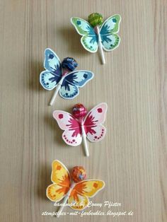 four colorful butterfly lollipops sitting on top of a wooden table next to each other