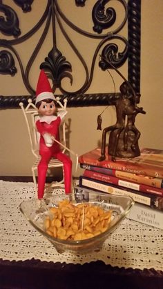 an elf sitting in a chair next to a bowl of cereal and some books on a table