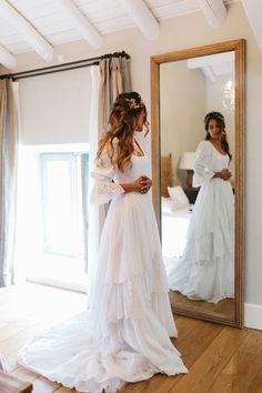 a woman standing in front of a mirror wearing a white dress and looking at her reflection