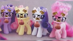 four little pony dolls wearing glasses and pink hair, one with gold rimmed glasses