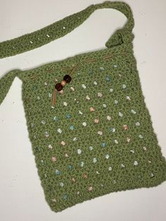 a green crocheted purse with buttons on the front and side, sitting on a white surface