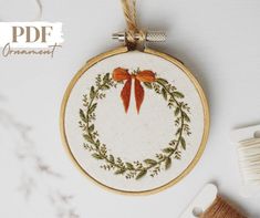 an embroidered christmas wreath ornament hanging on a white table with scissors and yarn