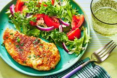 a blue plate topped with meat and salad next to a glass of green liquid on top of a table