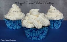 three cupcakes with white frosting and sprinkles sitting on a blue surface