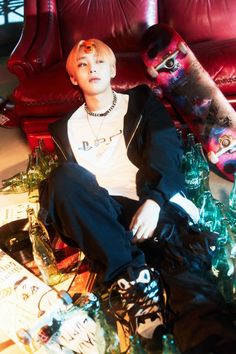 a young man sitting on the floor next to a skateboard and some glass bottles