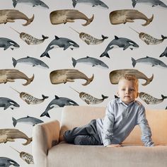 a young boy sitting on top of a couch next to a wall with dolphins painted on it