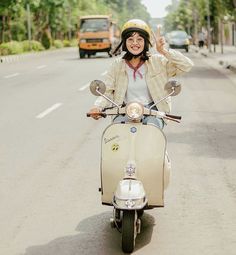 a woman riding on the back of a scooter down a street