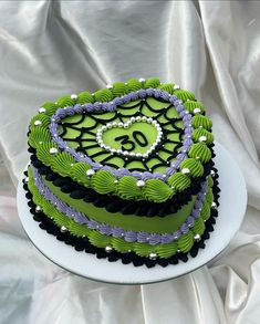 a green and black cake sitting on top of a white tablecloth covered table cloth