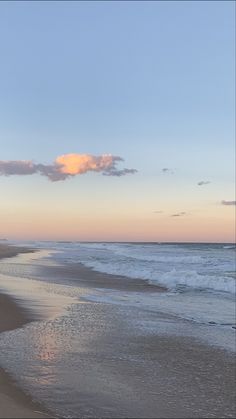 an empty beach with waves coming in to shore and the sun setting on the horizon