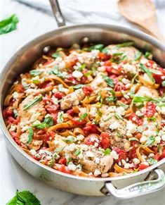 a skillet filled with pasta and meat covered in sauce, cheese and basil leaves