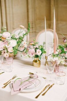 the table is set with pink and white flowers, gold place settings, and napkins