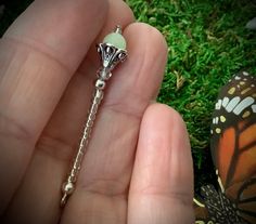 a hand holding a chain with a butterfly on it and a green bead around the end