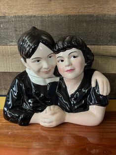 two ceramic figurines sitting next to each other on top of a wooden table