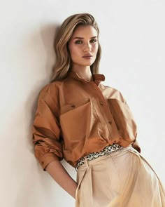 a woman leaning against a wall with her hands on her hips wearing a tan shirt and skirt