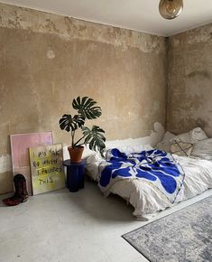 a bedroom with a bed, plant and pictures on the wall in it's corner