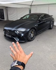 a person's hand next to a black car in a parking lot with a white tent