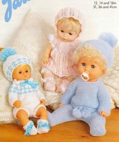 three little dolls sitting next to each other on a wooden floor with knitted blankets