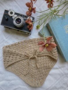 an old camera and some flowers on a bed next to a knitted cloth bag