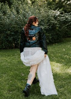 a woman sitting in the grass wearing a black leather jacket and white tulle skirt