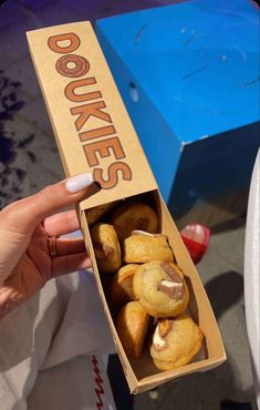 a person holding up a box filled with doughnuts on top of a table