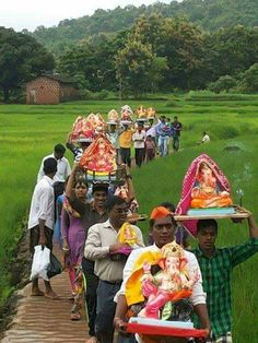 many people are walking in the grass carrying items on their heads and carrying trays