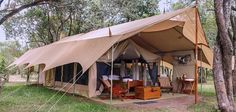 a tent in the woods with tables and chairs under it for people to sit outside