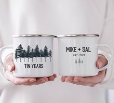 two people holding white mugs with trees printed on the front and back, in their hands